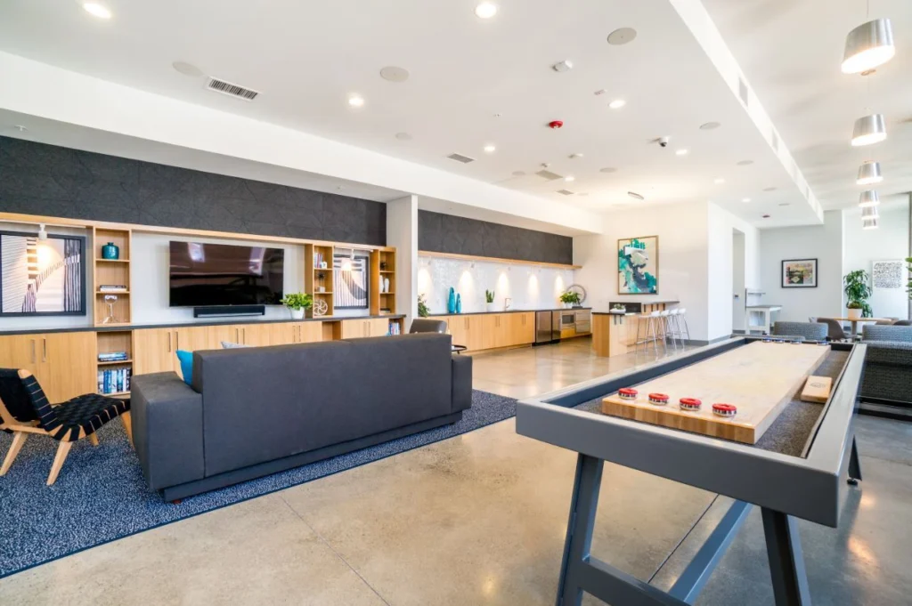 Clubhouse lounge with sofas, TV, kitchen, and shuffleboard table